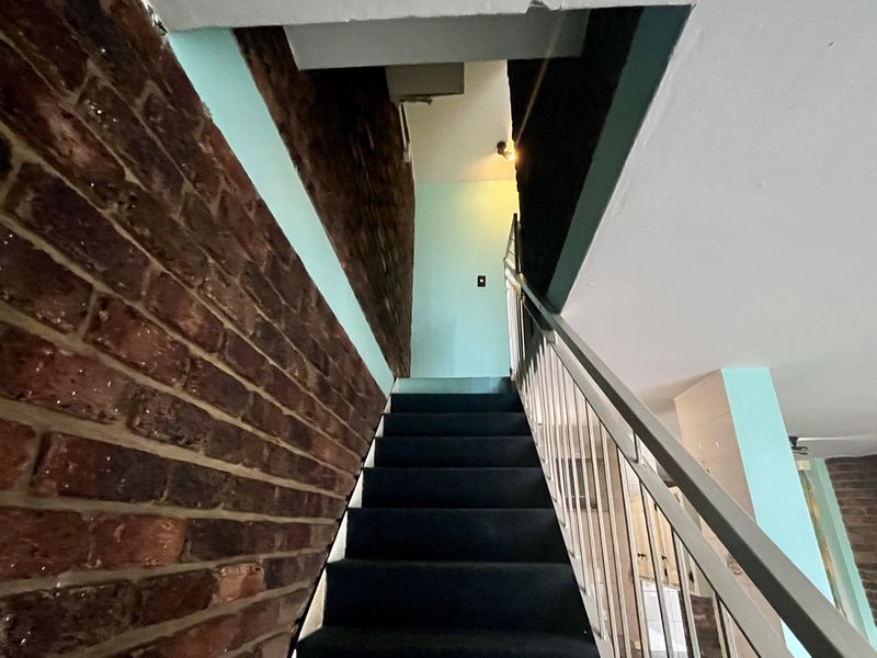 A staircase area featuring exposed brick walls and a metal railing, currently showing unfinished ceiling details and structural gaps.