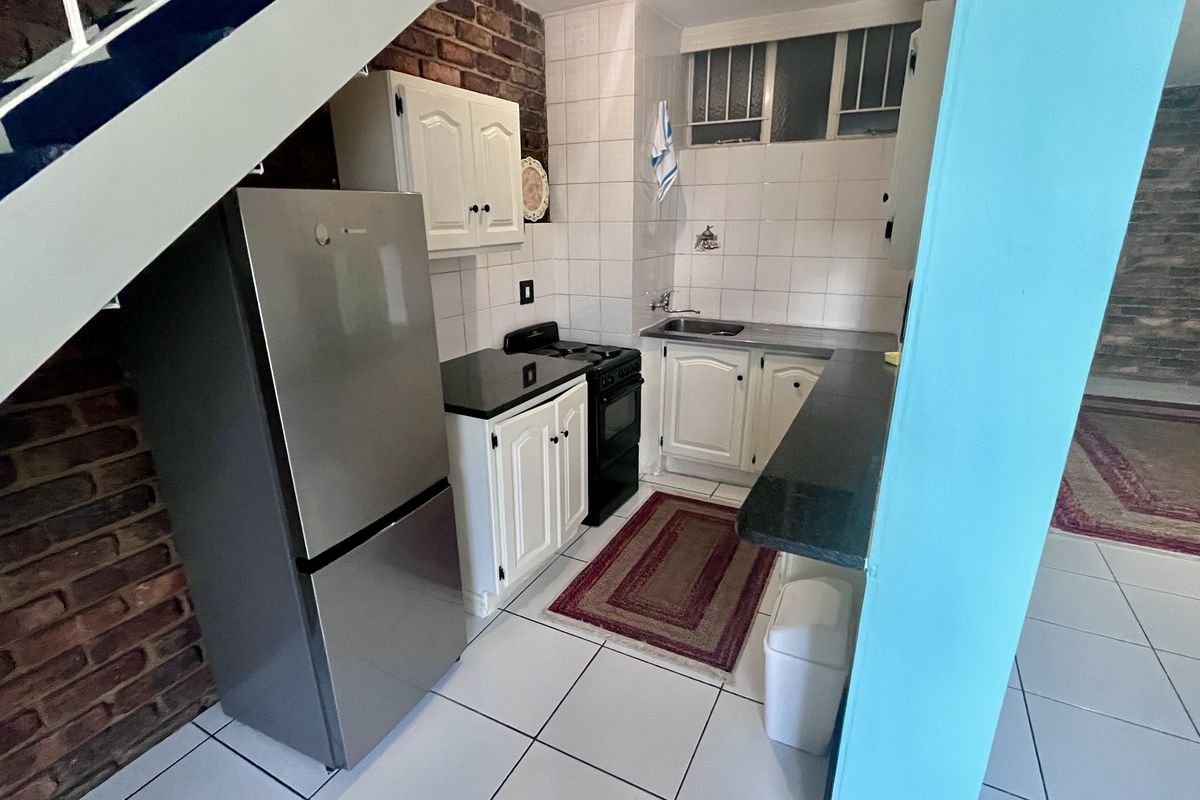 Compact kitchen featuring exposed brick walls, white cabinetry, tiled backsplash, and a functional layout with a stainless steel sink and stove.
