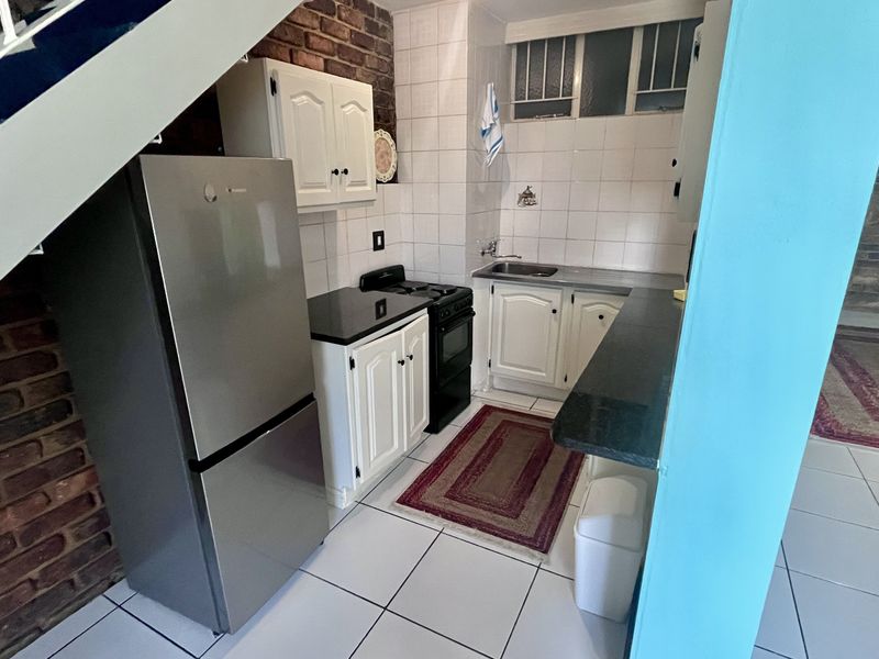 Compact kitchen featuring exposed brick walls, white cabinetry, tiled backsplash, and a functional layout with a stainless steel sink and stove.