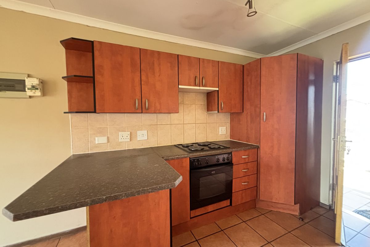 A functional kitchen featuring laminate cabinetry, a built-in oven and hob, tiled backsplash, and a breakfast bar, with direct access to the exterior.
