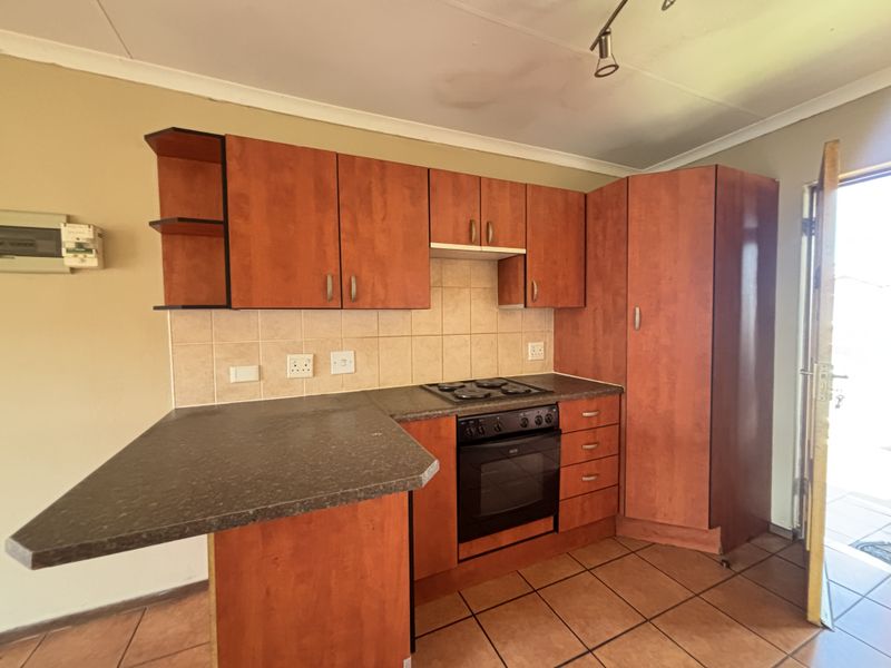 A functional kitchen featuring laminate cabinetry, a built-in oven and hob, tiled backsplash, and a breakfast bar, with direct access to the exterior.