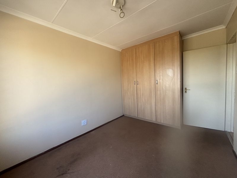 An empty bedroom featuring built-in wooden cupboards, carpeted flooring, and neutral wall finishes, offering a blank canvas for potential updates.