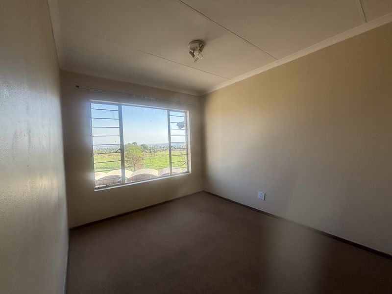 An empty bedroom featuring neutral walls, a large window with security bars, and a scenic outdoor view.
