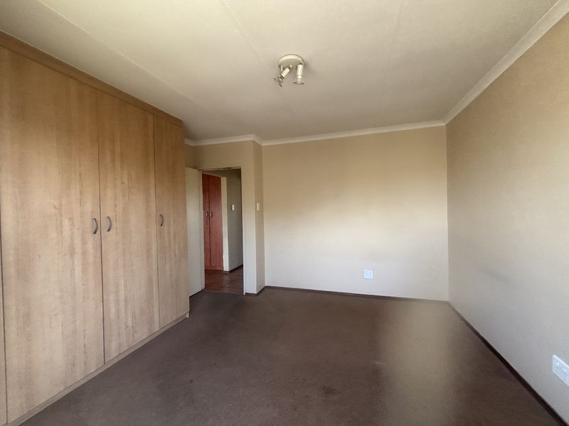A spacious, empty bedroom featuring built-in wooden cupboards, neutral wall finishes, and carpeted flooring, offering a blank canvas for personalization.