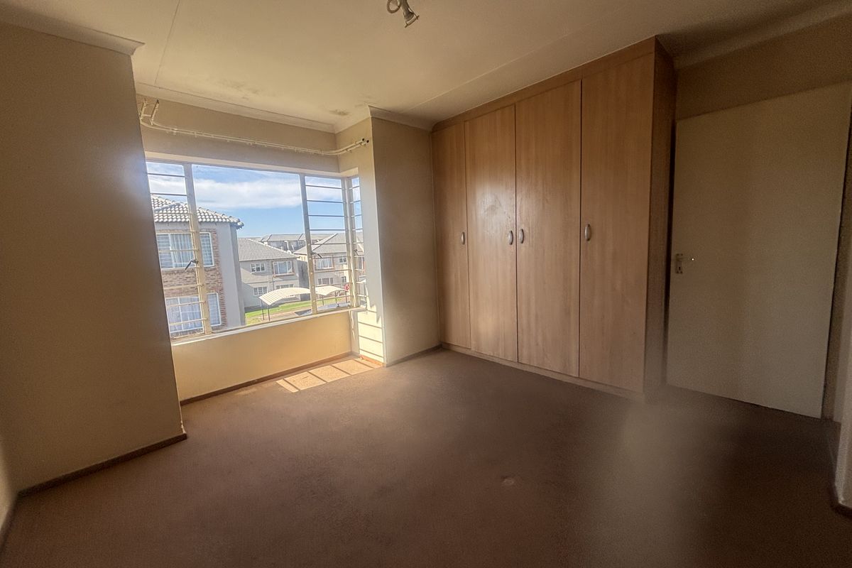 A spacious bedroom featuring built-in wooden cupboards and a large window with natural light, currently empty and ready for renovation.