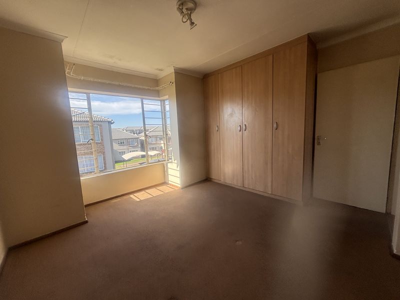 A spacious bedroom featuring built-in wooden cupboards and a large window with natural light, currently empty and ready for renovation.