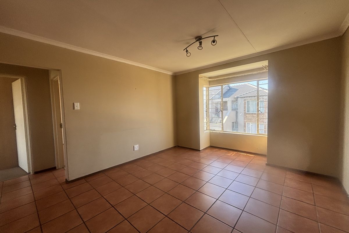A spacious, empty living room featuring neutral walls, ceramic tile flooring, and a large window providing natural light.