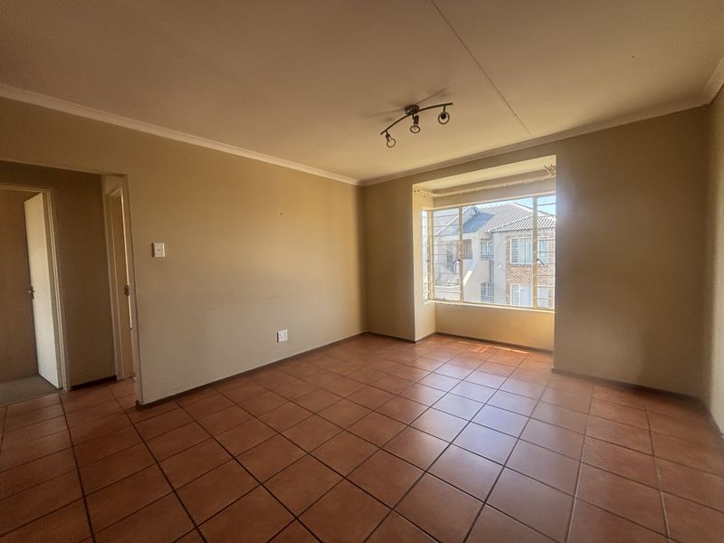 A spacious, empty living room featuring neutral walls, ceramic tile flooring, and a large window providing natural light.