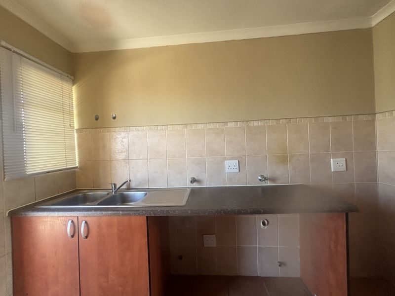 A functional kitchen area featuring a double bowl stainless steel sink, laminate countertop, tiled splashback, and built-in cabinetry with plumbing connections for appliances.