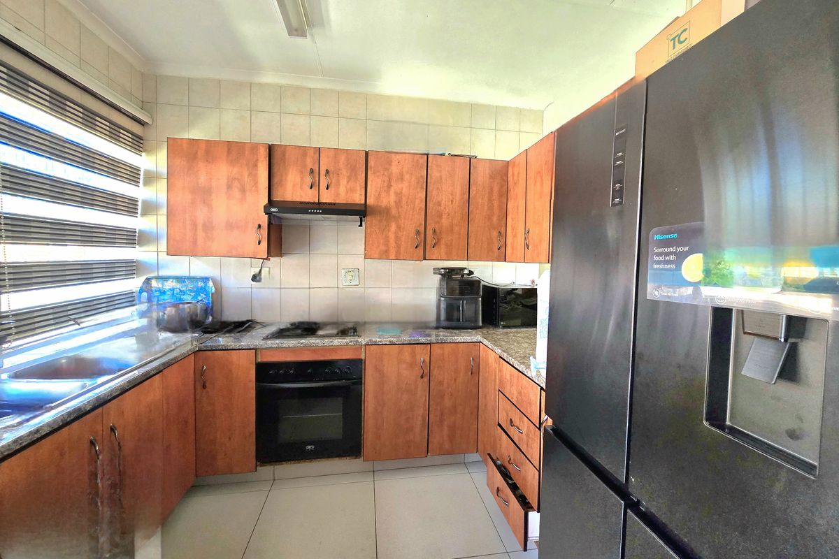 Functional kitchen featuring wood-finish cabinetry, granite countertops, built-in oven, hob, and extractor fan with tiled backsplash and flooring.