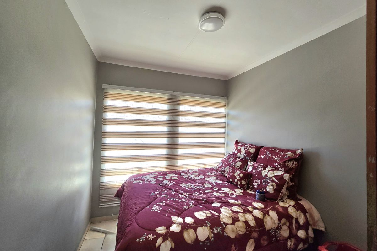 A compact bedroom featuring neutral wall paint, tiled flooring, and modern zebra blinds, providing a functional and well-lit sleeping space.