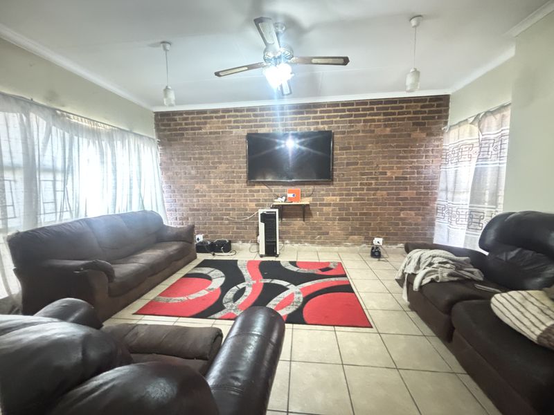 A living room featuring a prominent exposed brick feature wall, tiled flooring, and a ceiling fan, offering a solid foundation for modern updates.