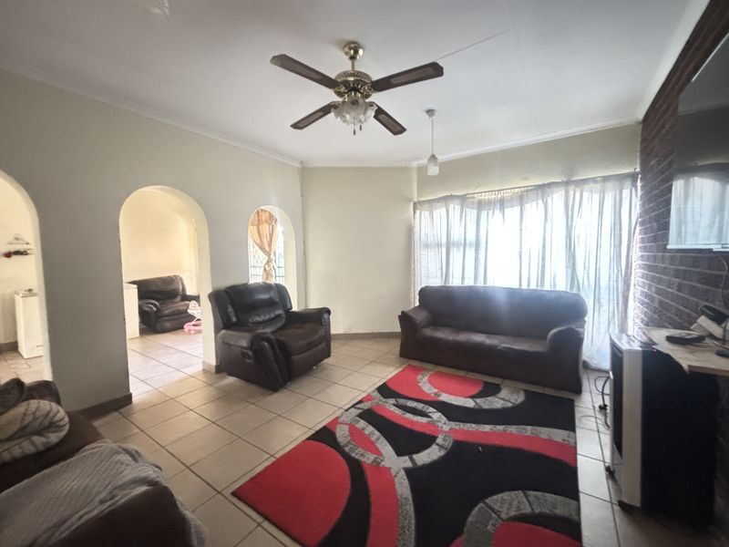A living room featuring tiled flooring, a ceiling fan, and an exposed brick feature wall with arched entryways leading to adjacent spaces.