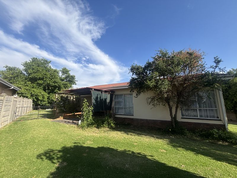 Rear view of the property featuring a lawn, covered patio area, and established garden with boundary walling.