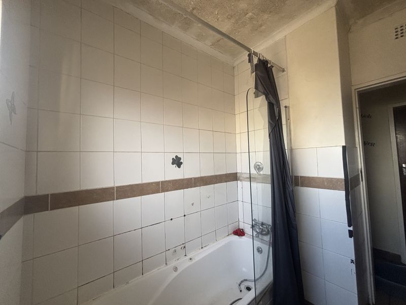A dated bathroom featuring a built-in bathtub with a shower screen, requiring cosmetic updates and ceiling repairs to restore its condition.