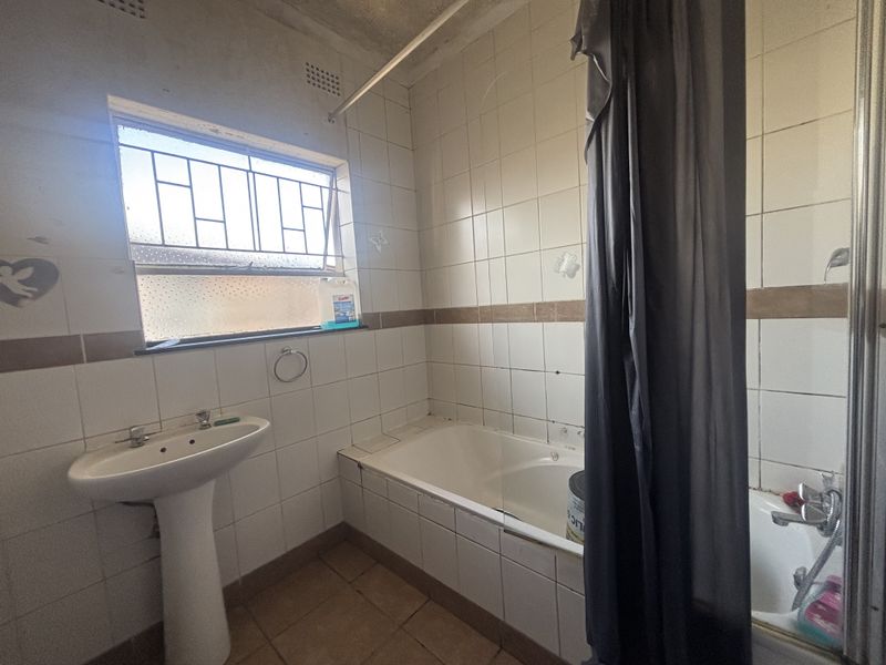 A dated bathroom featuring a pedestal basin, built-in bathtub, and tiled finishes, requiring cosmetic updates to improve its overall condition and appeal.