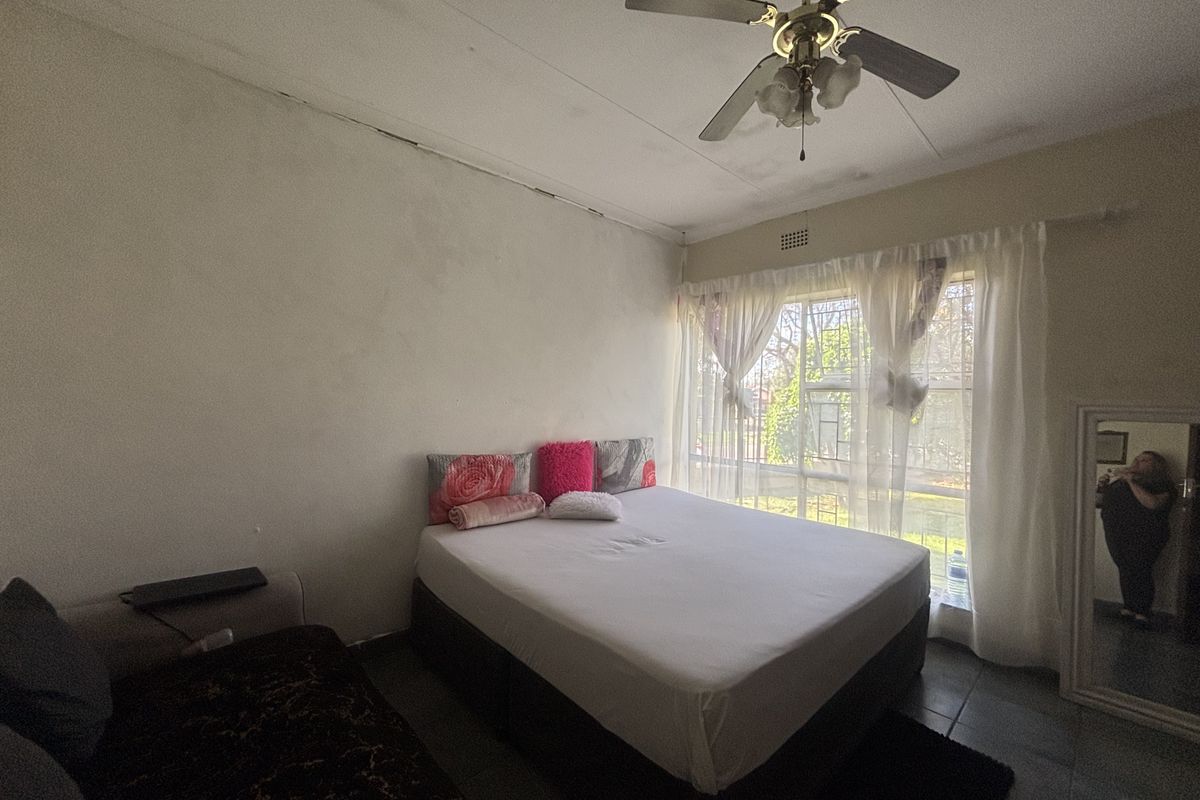 A bedroom featuring tiled flooring, a ceiling fan, and a window with security bars. The room requires cosmetic updates to the ceiling and walls.