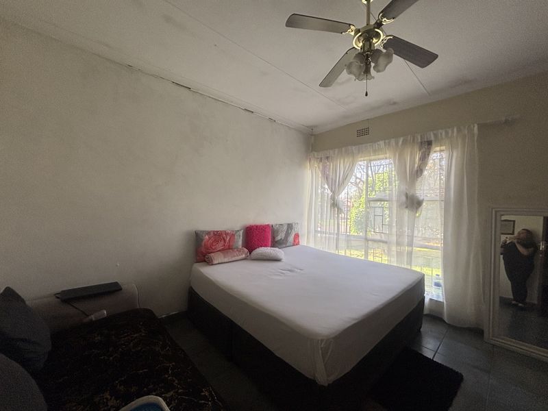A bedroom featuring tiled flooring, a ceiling fan, and a window with security bars. The room requires cosmetic updates to the ceiling and walls.