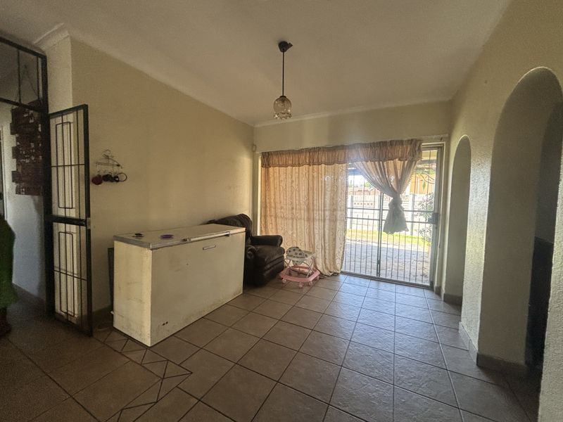 A living area featuring tiled flooring, an arched entryway, and a sliding glass door with an integrated security gate leading to the exterior.