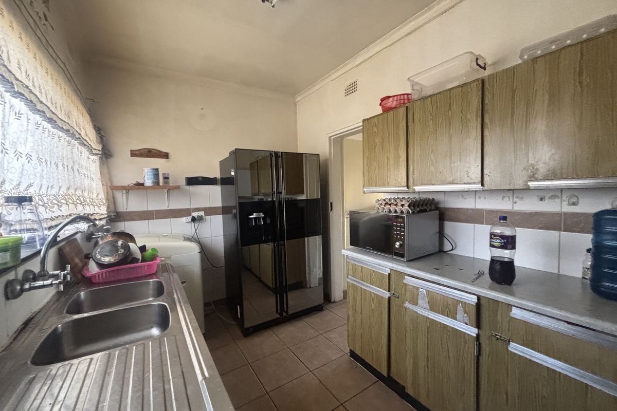 A dated kitchen featuring laminate cabinetry, tiled backsplash, and a double stainless steel sink, offering significant potential for modernization and renovation.