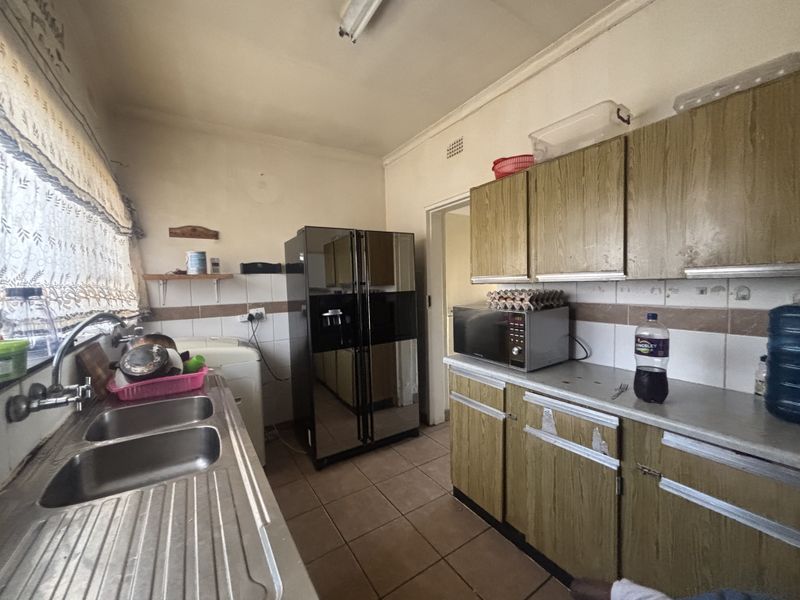 A dated kitchen featuring laminate cabinetry, tiled backsplash, and a double stainless steel sink, offering significant potential for modernization and renovation.