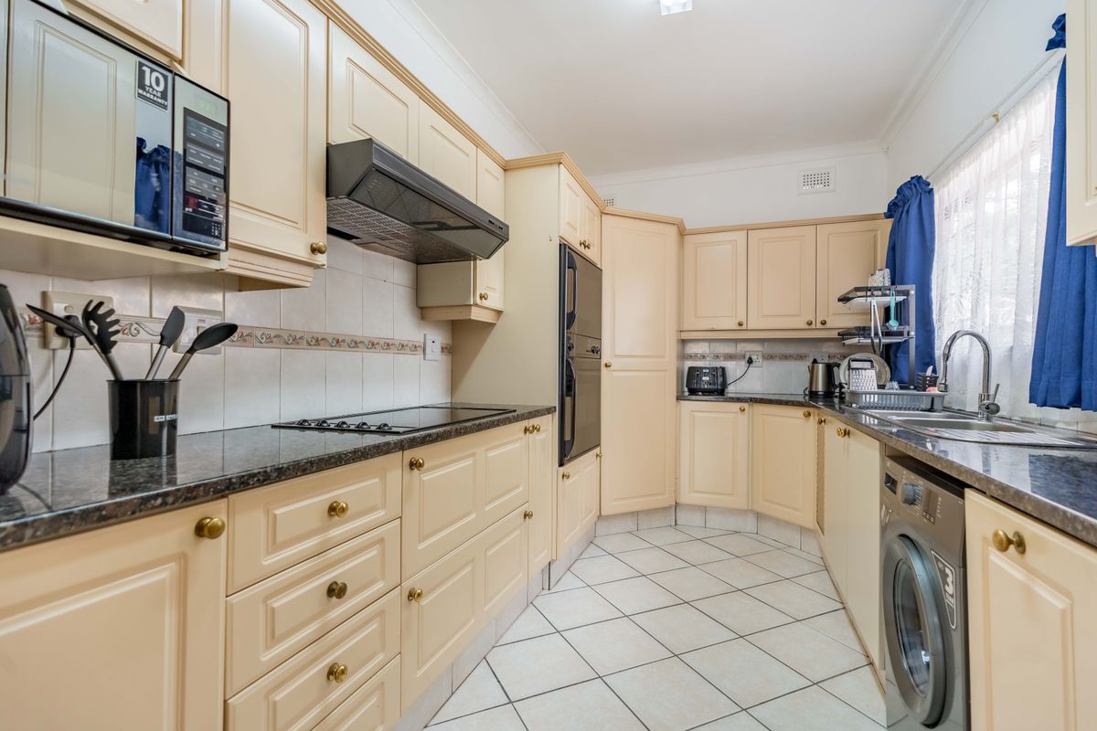 A functional kitchen featuring cream-toned cabinetry, dark laminate countertops, built-in appliances, and tiled flooring with a classic layout.