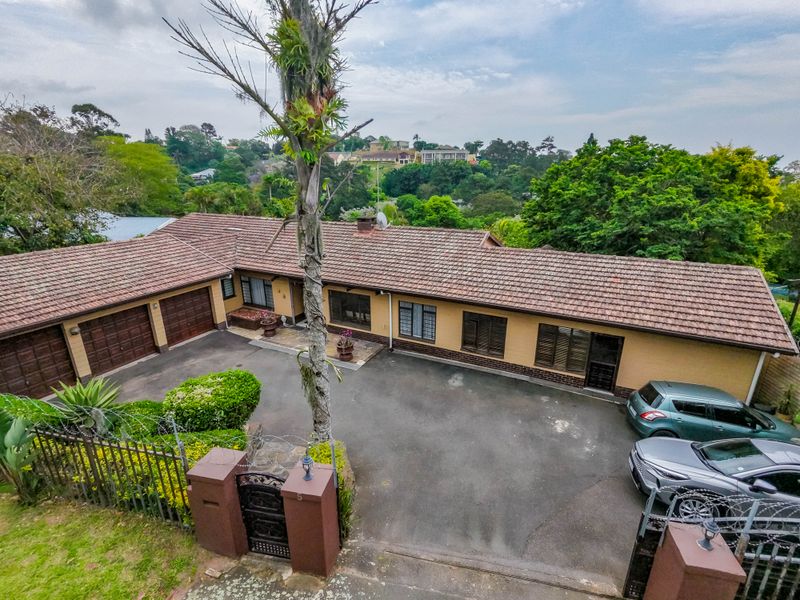 Elevated view of the front exterior featuring a brick facade, tiled roof, double garage, and paved driveway area.