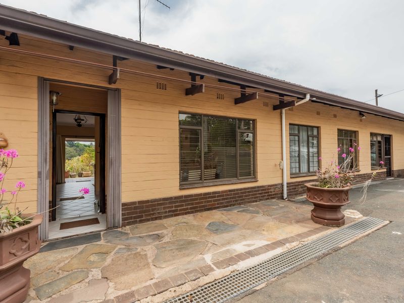 Front exterior view of the house featuring a stone paved patio, brick facade, and exposed timber rafters under a tiled roof.
