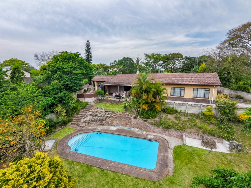 Aerial view of the rear garden featuring a swimming pool, stone retaining walls, and a covered patio area attached to the main residence.