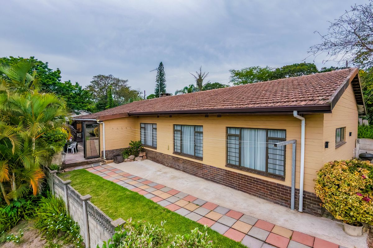 Rear view of the house featuring a tiled roof, brick facade, paved walkway, and a precast concrete boundary wall.