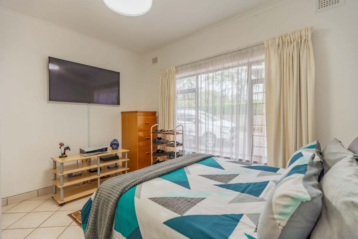 A functional bedroom featuring tiled flooring, a large window with curtains, and a wall-mounted television.