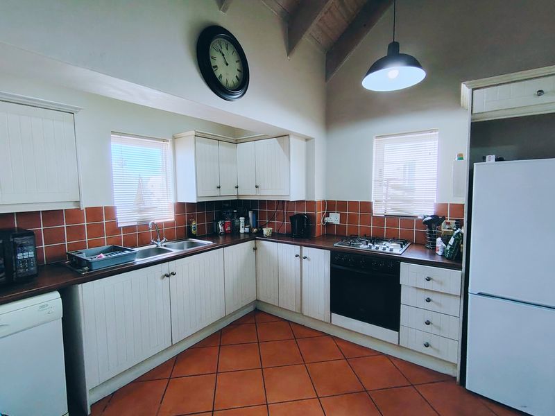 A functional kitchen featuring white cabinetry, a gas hob, built-in oven, tiled backsplash, and vaulted ceilings with pendant lighting.