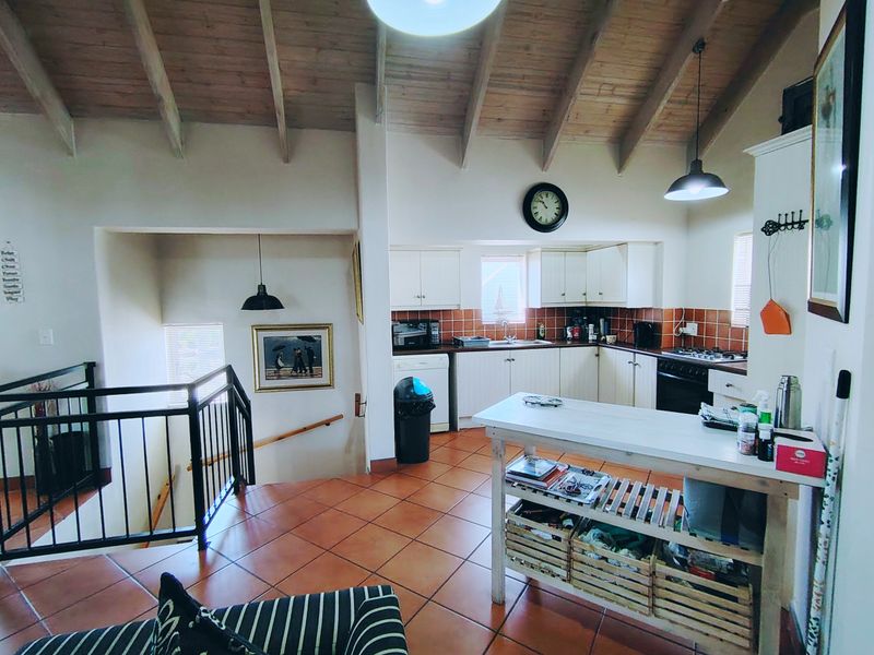 Open-plan kitchen and living area featuring vaulted timber ceilings, terracotta floor tiles, and a functional kitchen layout with built-in cabinetry and appliances.