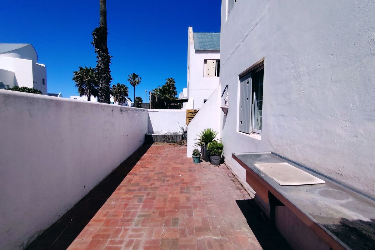 A private rear courtyard featuring brick paving, a built-in stainless steel prep counter, and high boundary walls, offering a functional outdoor utility space.