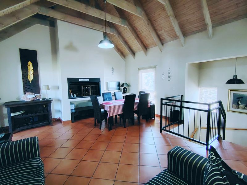 Spacious open-plan living and dining area featuring a high vaulted timber ceiling, exposed beams, terracotta flooring, and a built-in fireplace.