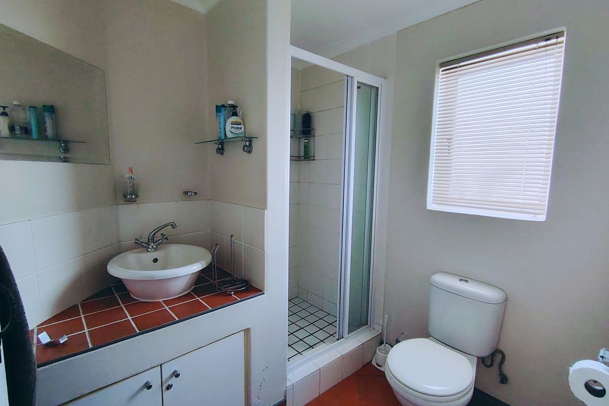 A functional bathroom featuring a corner vanity with tiled countertop, a separate shower enclosure, and a standard toilet.