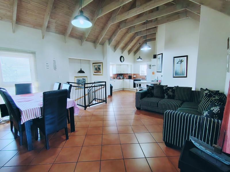 Spacious open-plan living and dining area featuring a vaulted timber ceiling with exposed beams, ceramic tile flooring, and an integrated kitchen.