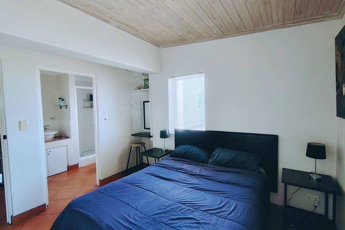 A bedroom featuring a timber ceiling, terracotta floor tiles, and an adjoining en-suite bathroom with a built-in vanity.