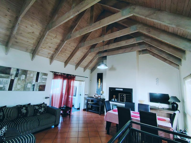 Spacious open-plan living and dining area featuring high vaulted ceilings with exposed timber trusses and a built-in fireplace.