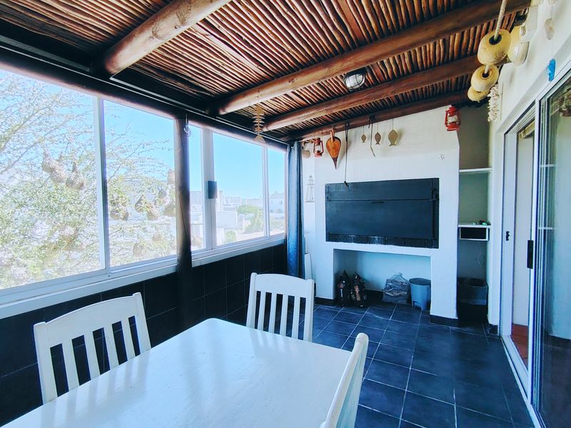 Enclosed patio area featuring a built-in braai, tiled flooring, and a rustic thatched ceiling with large sliding windows.