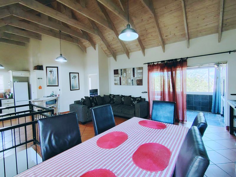 Spacious open-plan living and dining area featuring high exposed timber rafter ceilings, tiled flooring, and direct access to an outdoor balcony.