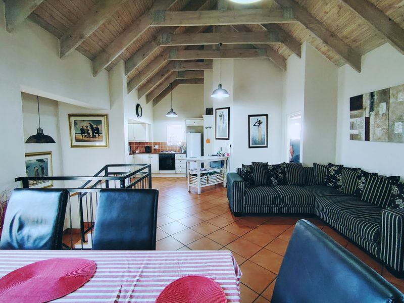 Spacious open-plan living and kitchen area featuring high vaulted ceilings with exposed timber rafters and classic terracotta floor tiles.