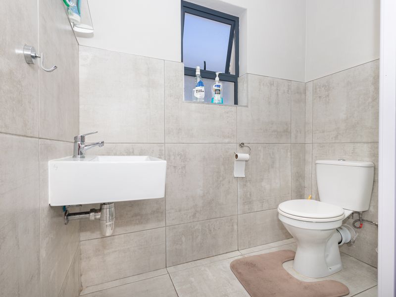 A modern, clean bathroom featuring a wall-mounted basin, chrome fixtures, and neutral floor-to-ceiling tiling with a functional top-hung window.