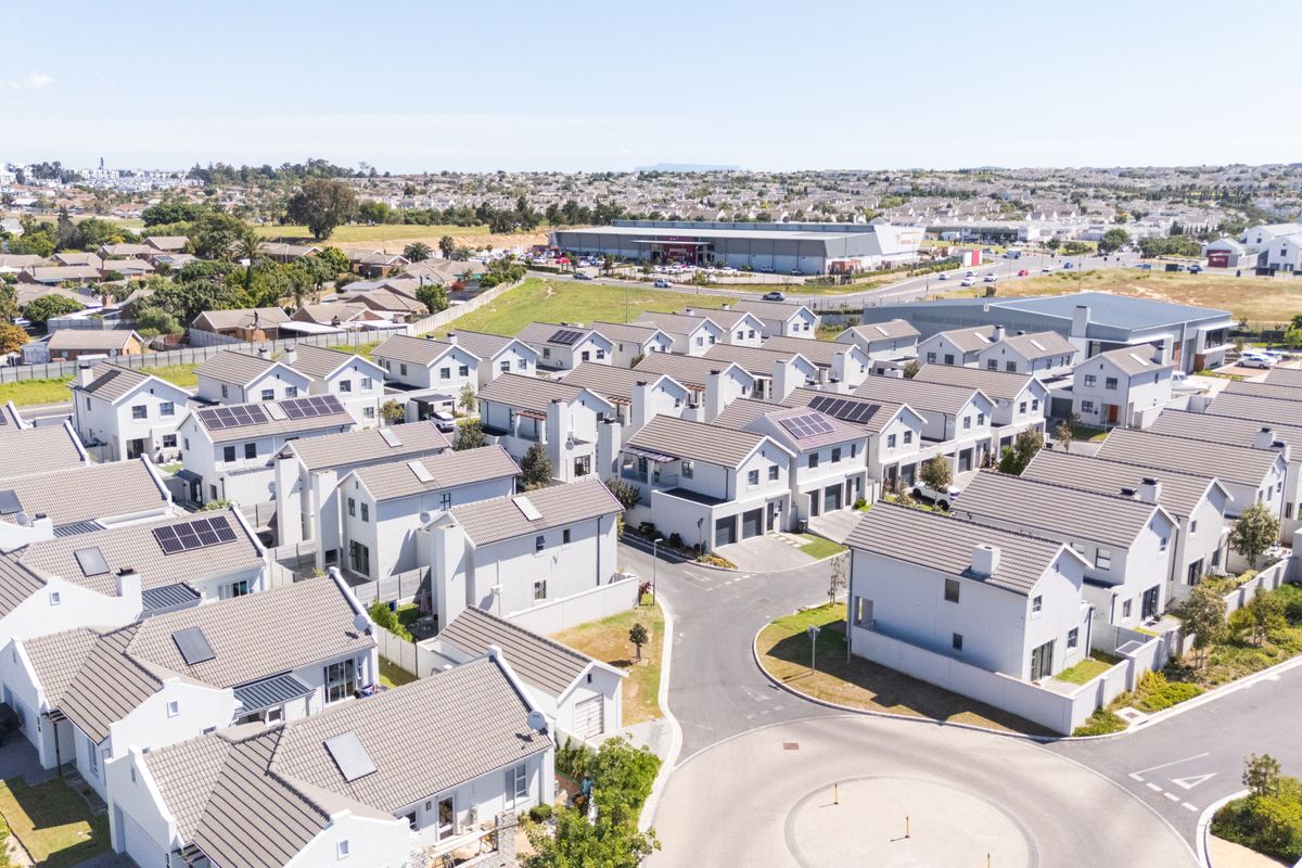 Aerial view of a modern townhouse complex featuring uniform architectural design, tiled roofs, integrated solar panels, and paved internal road infrastructure.