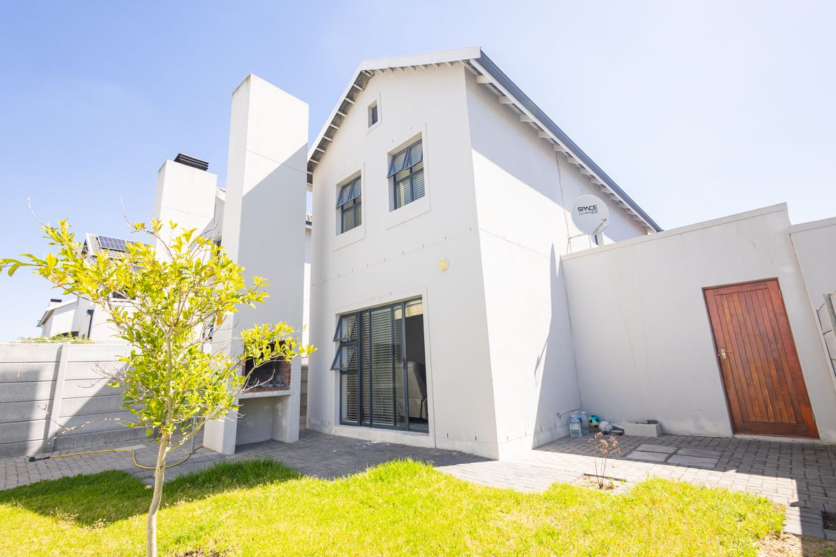 Rear exterior view of the townhouse featuring a paved patio area, built-in braai, and a small private garden space.