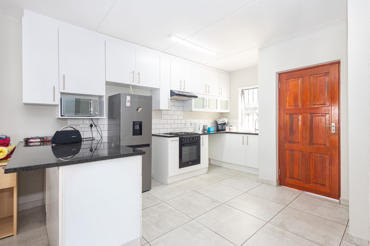 A well-maintained kitchen featuring white cabinetry, granite countertops, subway tile backsplash, and integrated appliances, complemented by neutral tiled flooring.
