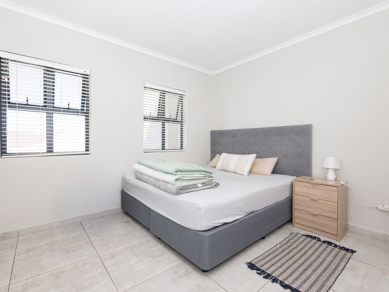 A bright and well-maintained bedroom featuring neutral tiled flooring, built-in cupboards, and venetian blinds, offering a clean and functional living space.