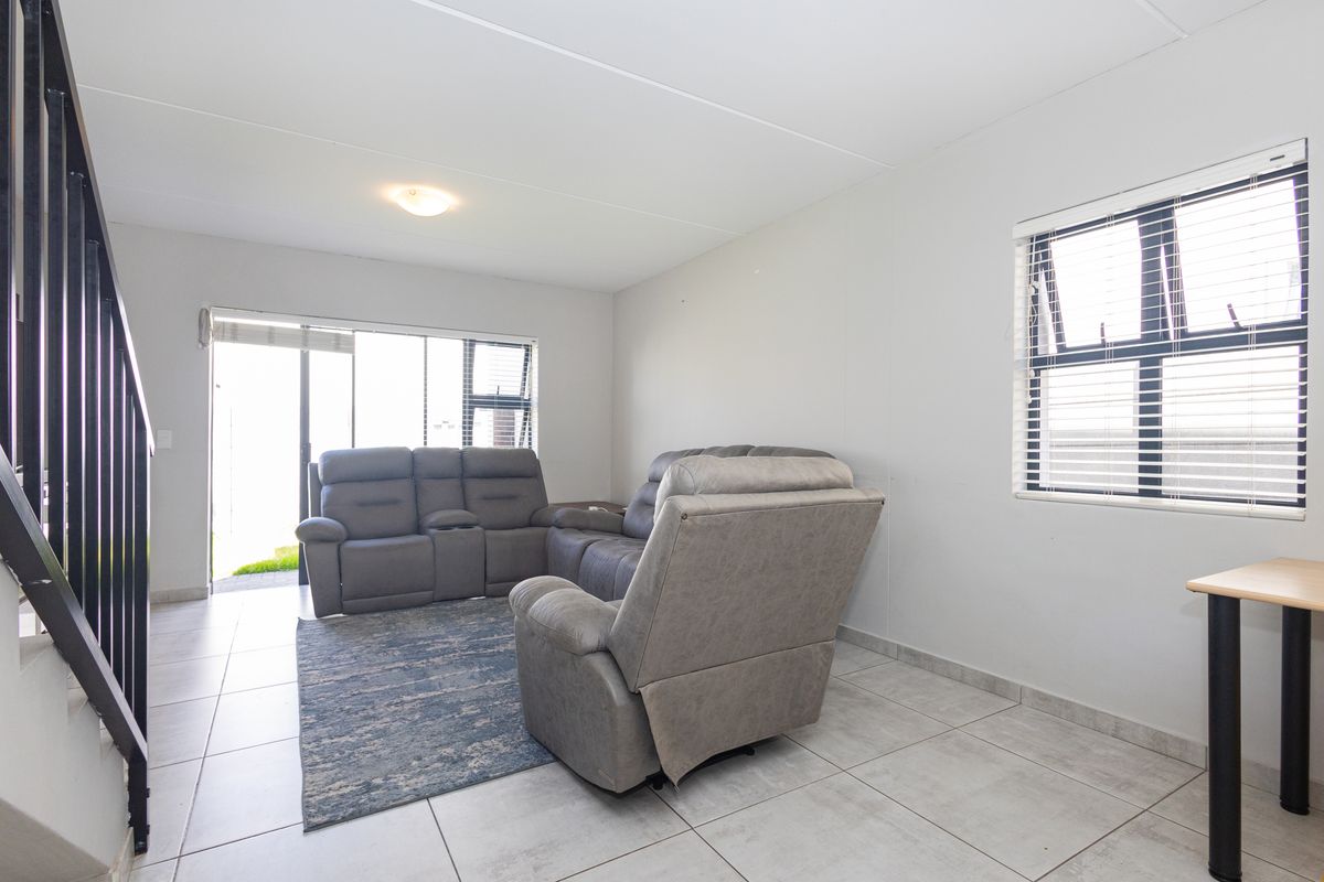 A bright living room featuring tiled flooring, a staircase with a metal balustrade, and access to the outdoors via a sliding glass door.