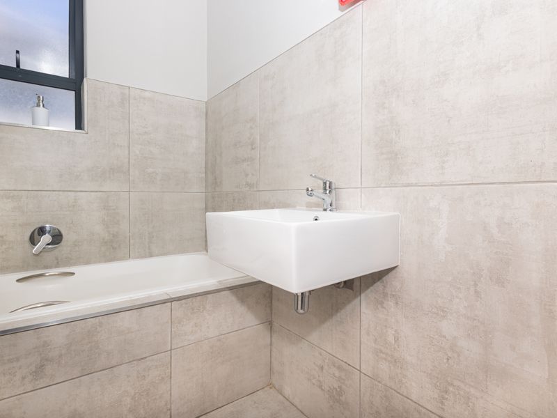 A modern, minimalist bathroom featuring a wall-mounted basin, built-in bathtub, and neutral large-format ceramic wall tiles.