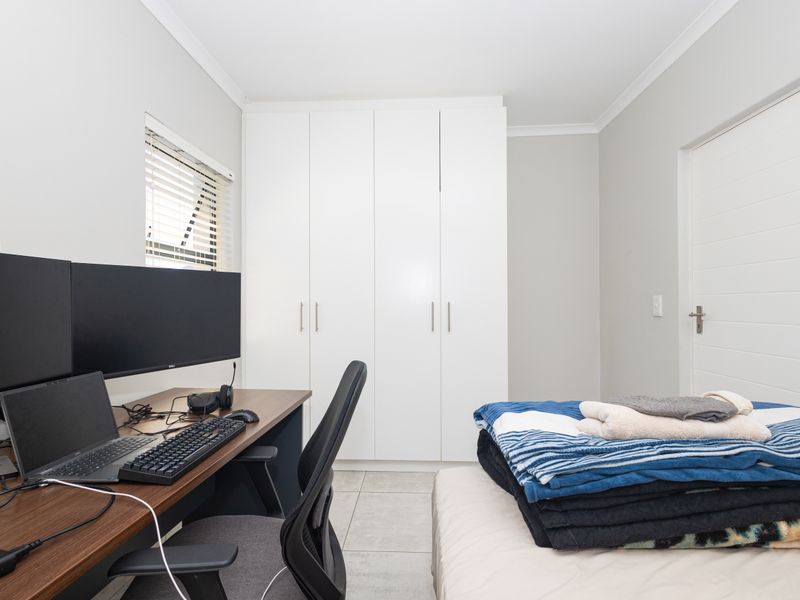 A functional bedroom featuring neutral wall tones, tiled flooring, and a spacious white built-in wardrobe, offering a clean and versatile living space.
